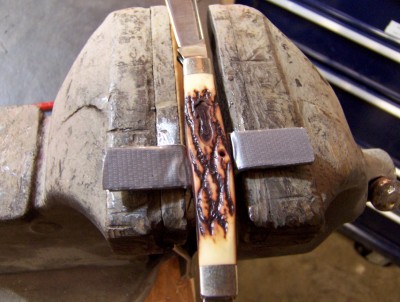 Place a knife in the vise with the blades open and tightened the bench vise until the backsprings of the knife are compressed.