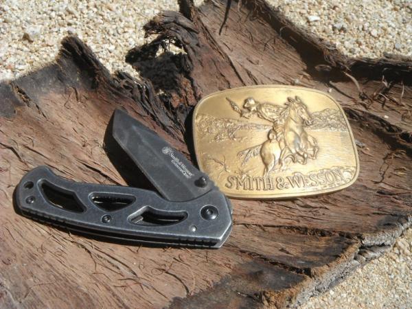 Smith & Wesson Folding knife CK404 & 1975 Smith & Wesson 'The Hostiles' Brass Belt Buckle. Smith & Wesson Folding knife CK404 & 1975 Smith & Wesson 'The Hostiles' Brass Belt Buckle.