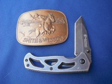 Smith & Wesson Folding knife CK404 & 1975 Smith & Wesson 'The Hostiles' Brass Belt Buckle. Smith & Wesson Folding knife CK404 & 1975 Smith & Wesson 'The Hostiles' Brass Belt Buckle.