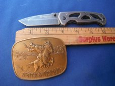 Smith & Wesson Folding knife CK404 & 1975 Smith & Wesson 'The Hostiles' Brass Belt Buckle. Smith & Wesson Folding knife CK404 & 1975 Smith & Wesson 'The Hostiles' Brass Belt Buckle.