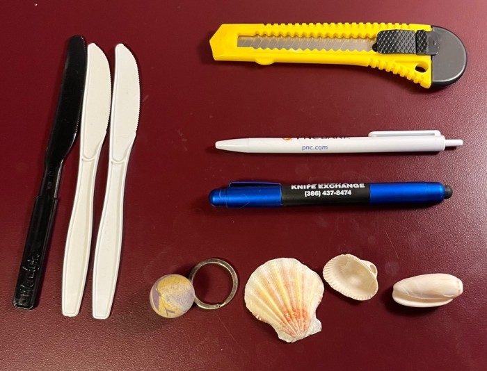 As assortment of plastic knives, box cutter, a rubber ball, and sea shells