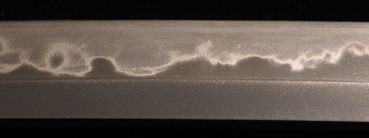 Hamon line from differentially heat treating. This looks like clay was used to create a hamon, not even, like it was in fluid only